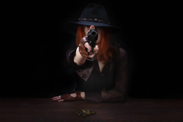 Wild west girl with revolver gun sitting at the table with ammunition and silver coins — Stock Photo, Image