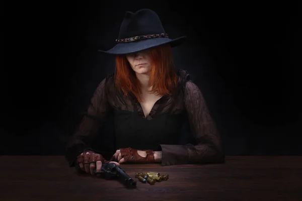 Vilda västern flicka med revolver pistol sitter vid bordet med ammunition och silvermynt — Stockfoto