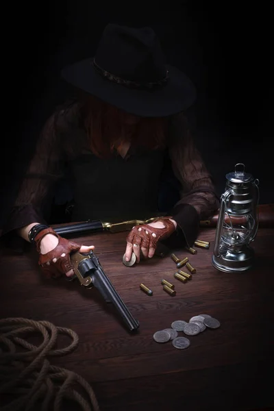 Девушка с револьвером, сидящая за столом с боеприпасами и серебряными монетами — стоковое фото