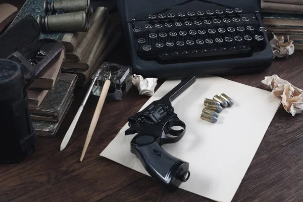 写一个犯罪小说故事- -老式复古打字机和左轮手枪，配有弹药、书籍、空白纸、墨笔 — 图库照片