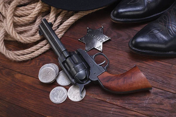 Old western gun with sheriff badge and silver dollars with hat, rope and boots — Stock Photo, Image