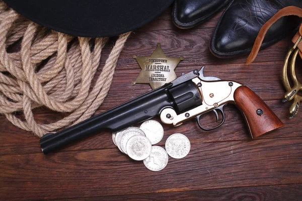 Old western gun with marshal badge and silver dollars with hat, rope and boots — Stock Photo, Image