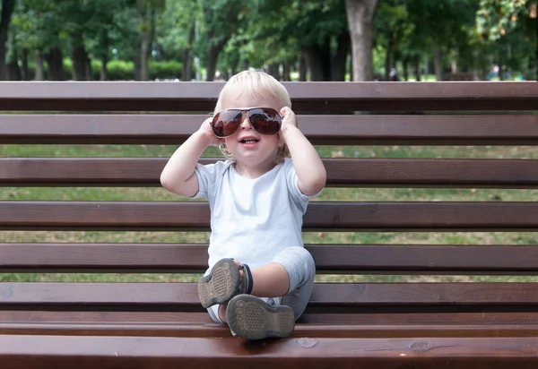 Sitting child with sun glasses, blondidan with blue eyes on a wo — Stock Photo, Image