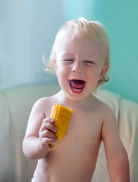 Little baby holds corn and laughs, white-skinned toddler with wh — Stock Photo, Image