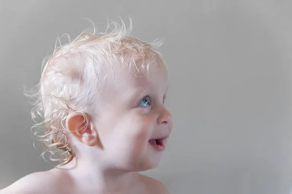 Curly baby in profile, portrait of a smiling child on a gray bac — Stock Photo, Image