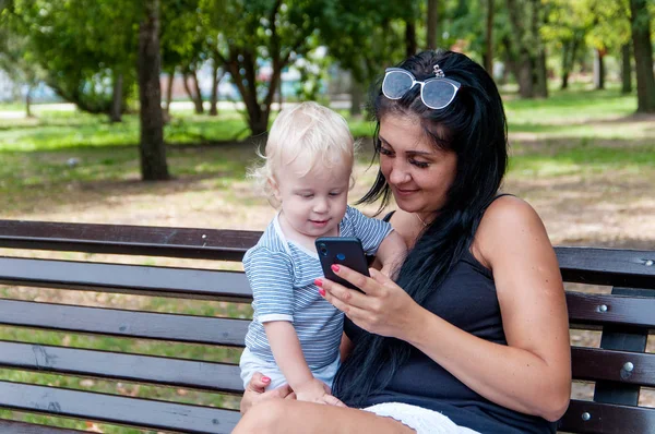 Ребенок, сидящий на руках у матери, смотрит в телефон — стоковое фото