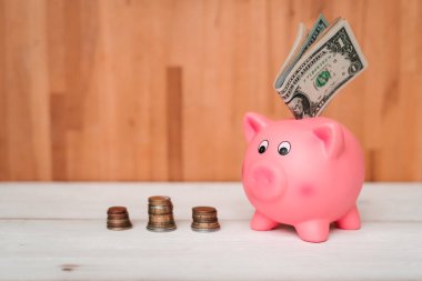 Küçük şirin pembe domuz kumbara ahşap bir masa üzerinde. Üç yığın, sent ve kağıt dolar. Tasarruf ve finans.