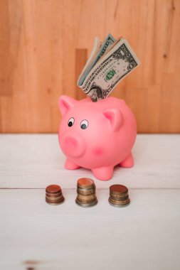 Küçük şirin pembe domuz kumbara ahşap bir masa üzerinde. Üç yığın, sent ve kağıt dolar. Tasarruf ve finans.
