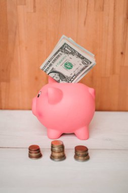 Küçük şirin pembe domuz kumbara ahşap bir masa üzerinde. Üç yığın, sent ve kağıt dolar. Tasarruf ve finans.