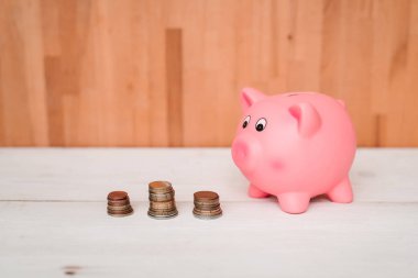 Küçük şirin pembe domuz kumbara ahşap bir masa üzerinde. Üç yığın, sent ve kağıt dolar. Tasarruf ve finans.