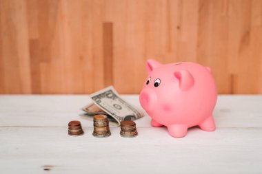 Küçük şirin pembe domuz kumbara ahşap bir masa üzerinde. Üç yığın, sent ve kağıt dolar. Tasarruf ve finans.
