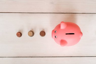 Küçük şirin pembe domuz kumbara ahşap bir masa üzerinde. Üç yığın, sent ve kağıt dolar. Tasarruf ve finans.