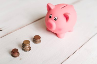 Küçük şirin pembe domuz kumbara ahşap bir masa üzerinde. Üç yığın, sent ve kağıt dolar. Tasarruf ve finans.