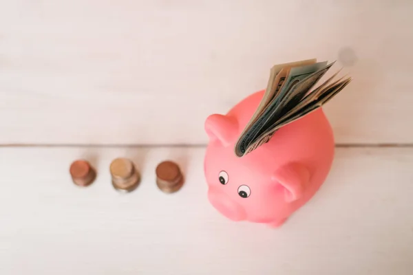 Küçük şirin pembe domuz kumbara ahşap bir masa üzerinde. Üç yığın, sent ve kağıt dolar. Tasarruf ve finans.