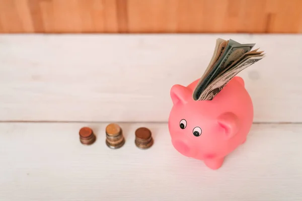 Küçük şirin pembe domuz kumbara ahşap bir masa üzerinde. Üç yığın, sent ve kağıt dolar. Tasarruf ve finans.