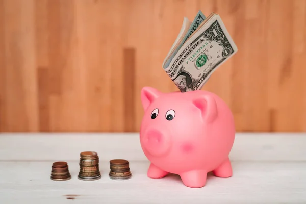 Küçük şirin pembe domuz kumbara ahşap bir masa üzerinde. Üç yığın, sent ve kağıt dolar. Tasarruf ve finans.