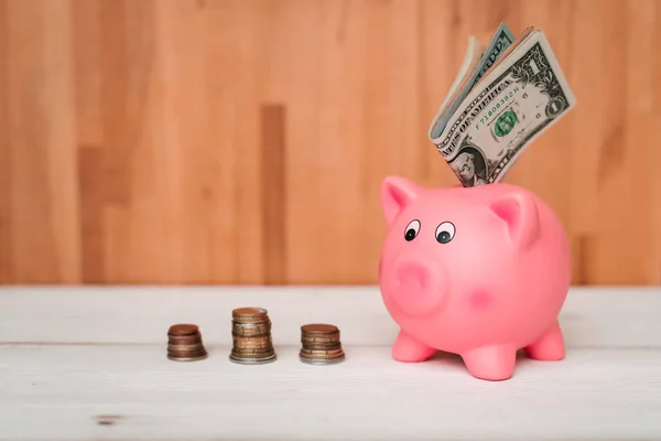 Küçük şirin pembe domuz kumbara ahşap bir masa üzerinde. Üç yığın, sent ve kağıt dolar. Tasarruf ve finans.