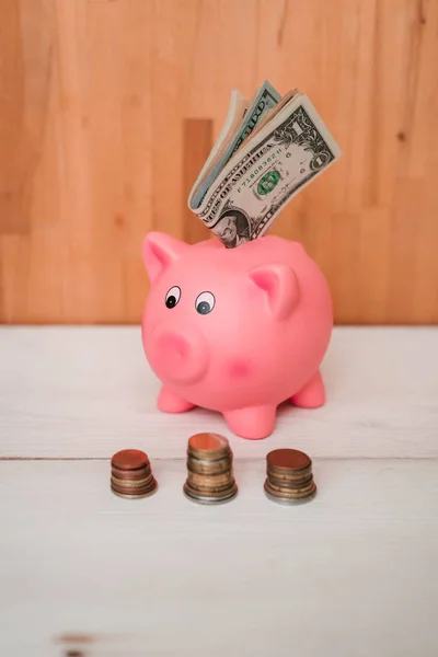 Küçük şirin pembe domuz kumbara ahşap bir masa üzerinde. Üç yığın, sent ve kağıt dolar. Tasarruf ve finans.