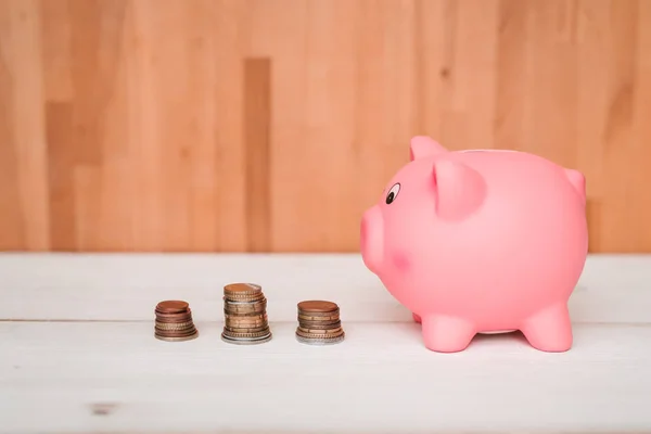 Küçük şirin pembe domuz kumbara ahşap bir masa üzerinde. Üç yığın, sent ve kağıt dolar. Tasarruf ve finans.