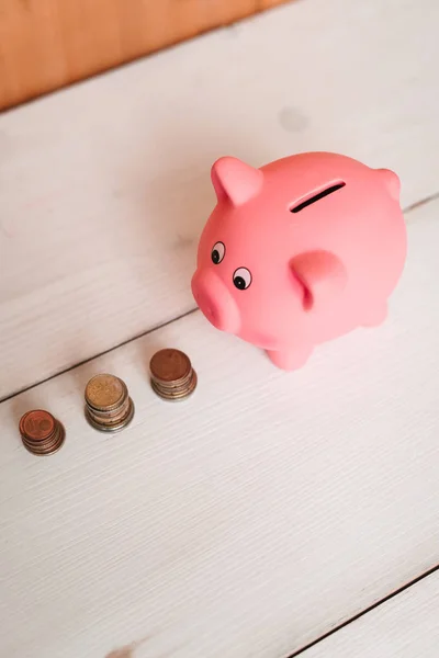 Küçük şirin pembe domuz kumbara ahşap bir masa üzerinde. Üç yığın, sent ve kağıt dolar. Tasarruf ve finans.