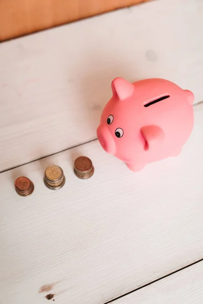 Küçük şirin pembe domuz kumbara ahşap bir masa üzerinde. Üç yığın, sent ve kağıt dolar. Tasarruf ve finans.