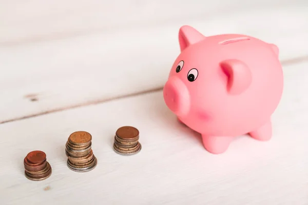 Küçük şirin pembe domuz kumbara ahşap bir masa üzerinde. Üç yığın, sent ve kağıt dolar. Tasarruf ve finans.