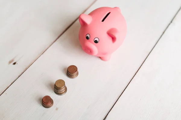 Küçük şirin pembe domuz kumbara ahşap bir masa üzerinde. Üç yığın, sent ve kağıt dolar. Tasarruf ve finans.
