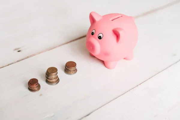 Küçük şirin pembe domuz kumbara ahşap bir masa üzerinde. Üç yığın, sent ve kağıt dolar. Tasarruf ve finans.