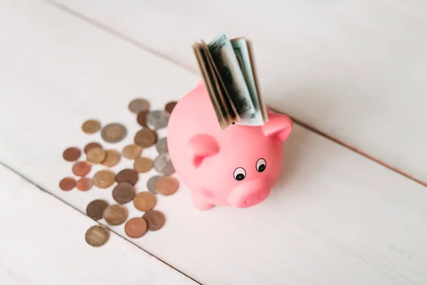 Küçük şirin pembe domuz kumbara ahşap bir masa üzerinde. Üç yığın, sent ve kağıt dolar. Tasarruf ve finans.