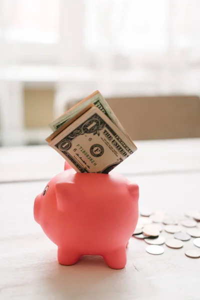 Küçük şirin pembe domuz kumbara ahşap bir masa üzerinde. Üç yığın, sent ve kağıt dolar. Tasarruf ve finans.