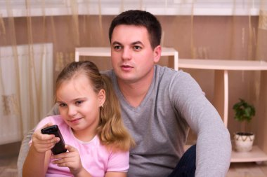 adam ve genç kız gülümseyerek uzaktan kumanda ile oturma odasında