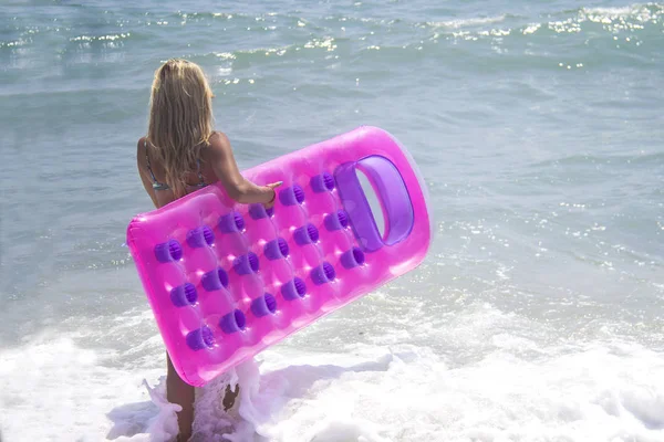 穿着蓝色比基尼的赤脚女孩在海边 穿泳装的身材苗条的女孩穿着粉红色的充气泳池筏在海里漫步 — 图库照片