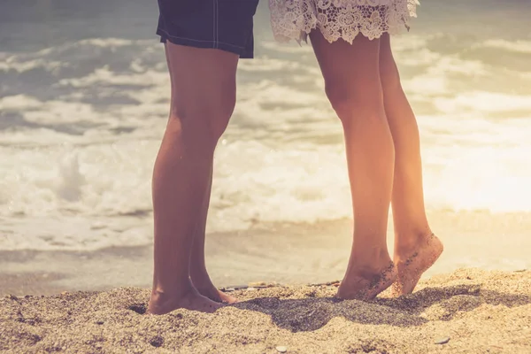 若いカップル ビーチの砂に足です 熱帯の夏の休日を旅行します キスの新婚夫婦恋人が海の前でハグの日没のシルエット — ストック写真