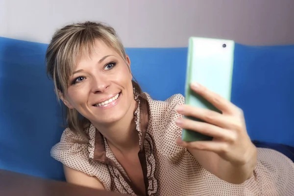 Cute Blond Girl Sofa She Looks Her Smartphone Makes Selfie — Stock Photo, Image