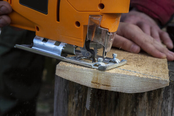 Человек режет деревянные изделия, используя электропилы на открытом воздухе. Крупный план
