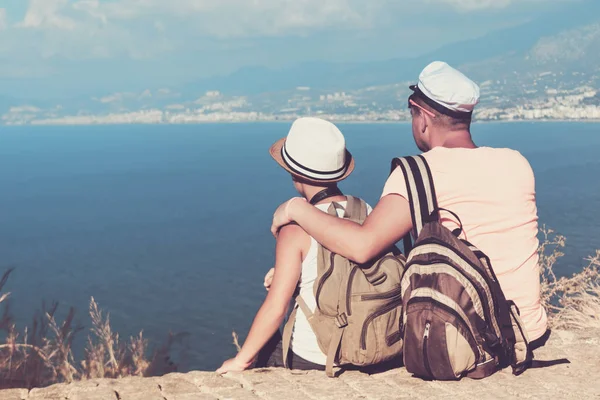 若い父親とバックパックの息子は 海の背景にビーチに座っています 家族旅行の概念 — ストック写真