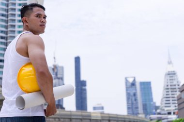 Asya adam işçi emek sarı zor kask ve arka plan üzerinde şehir ile plan holding inşaat sitesinde.