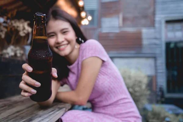 Woman cheers drinking beer bottle. Young girl clinking toast alcohol in bar. Lady people party in club having fun. Asian female give beer bottle to you.