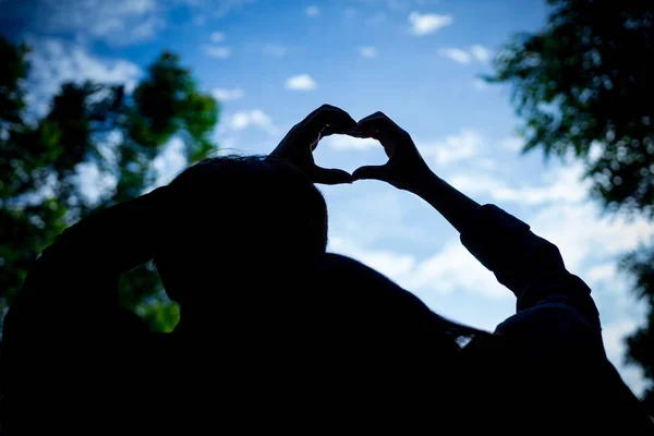 Silhouette Couple Hands in shape of love heart in blue sky. Lovers makes heart symbol in nature outdoor.