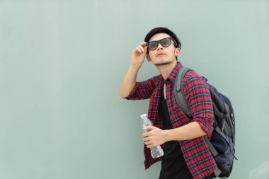 Dikey moda yakışıklı Asya adam gri arka plan üzerinde. Hipster seyahat sırt çantası Plastik holding ile şişe su ve güneş gözlüğü ayarlayın. Genç erkek turist uzun yürüyüşe çıkan kimse seyahat etmek tatil kavramı.