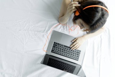 Laptop beyaz yatakta sabah tipik bir kadın. Genç Asyalı kız evde müzik dinleme dizüstü bilgisayar kullanarak. Mutlu erkek laptop internet ile film izlerken kulaklık kullanın. insanlar teknoloji kavramı.