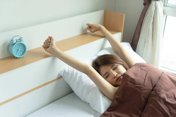 Young woman stretch arms in the air with alarm clock. wake up early in morning. Girl stop snooze alarm. female waking up sleepy and tired. woman wake up in the morning with alarm clock snooze.