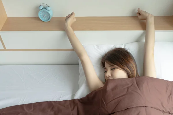Young woman stretch arms in the air with alarm clock. wake up early in morning. Girl stop snooze alarm. female waking up sleepy and tired. woman wake up in the morning with alarm clock snooze.