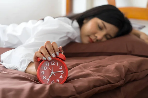 Young woman holding alarm clock on bed. wake up early in morning. Girl stop snooze alarm. female waking up sleepy and tired. woman wake up in the morning with alarm clock snooze concept.