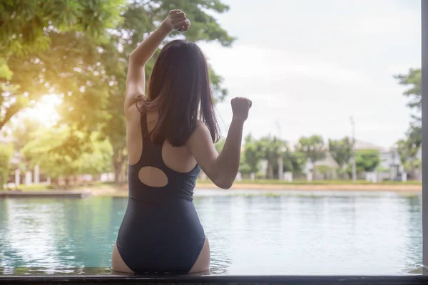 Young woman sitting at swimming pool, back view. Asian girl in bikini rear view.