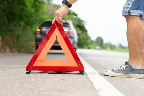 Araba arızası yolun yanında adam uyarı üçgeni ayarlar.