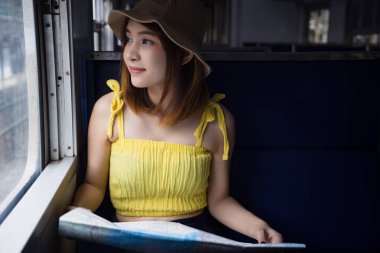 Tren istasyonunda harita tutarak tren oturan genç Asyalı kadın. Bayan yolcu pencereden dışarı bakarak trenle seyahat. Tatil tatil gezi kavramı.