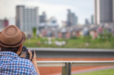 Genç Asian traveler altında giyiyor şapka alarak fotoğraf dslr kamera ile şehir Bangkok, Thailan arka planda Bina iş bölgesi ile adam