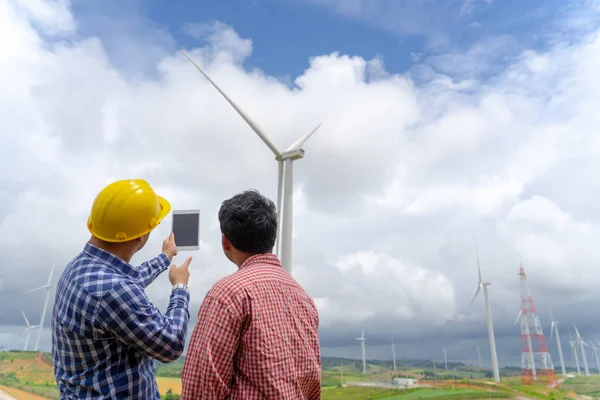 architecture businessman talking with partner about wind turbine farm project on tablet, technology renewable power indusrty concept.