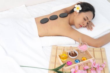 Tay kadın sırtsiyah sıcak taş ile spa salonunda beyaz yatakta kapanış gözleri aşağı yatarken. spa aromaterapi cilt bakımı gevşeme kavramı.